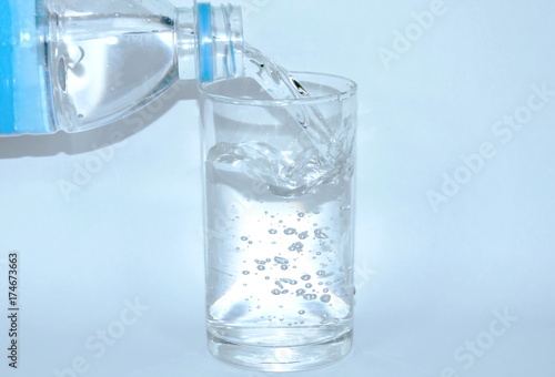 water pouring from bottle in drinking glass on white background