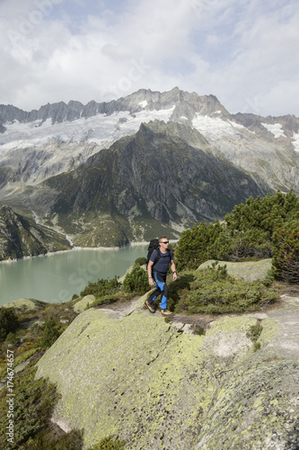 Hiker hikes through a wild high alpine landscape with a lake and glacier in the background, Switzerland