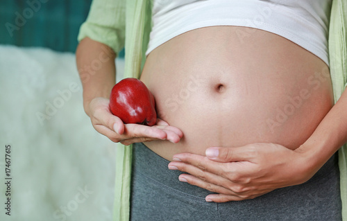 Pregnant woman holding Red Apple fruit at her belly.