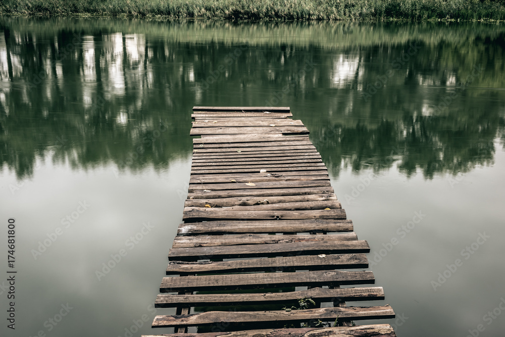 Obraz premium Pier on a calm river in the summer. Wooden pier bridge in the morning. Place for fishing in the river. Toned, style photo.