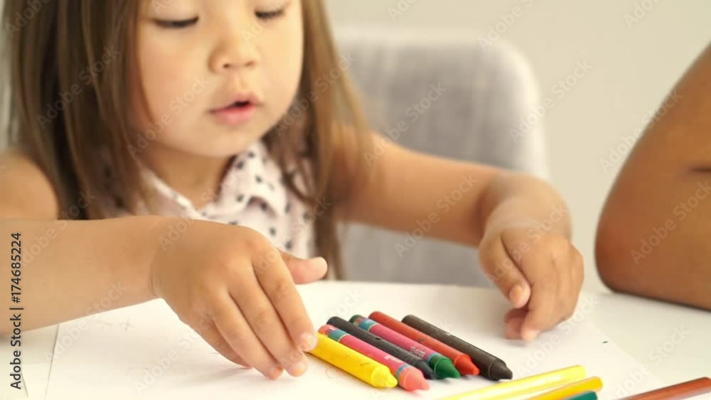 Close up view of Happy young girl sitting by the table at home with her mother and playing with her markers Close up view of Happy young girl sitting by the table at home with her mother and playing with her markers