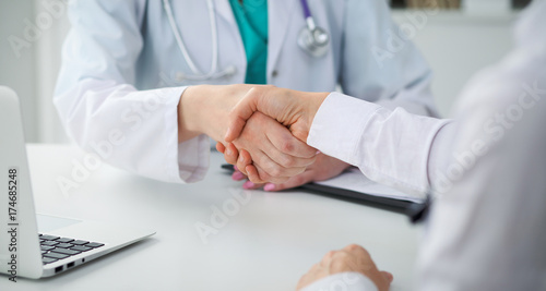 Doctor and patient shaking hands, close-up. Physician talking about medical examination results. Medicine, healthcare and trust concept