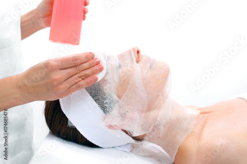 Pielęgnacja skóry twarzy w gabinecie kosmetycznym. Kosmetyczka nakłada preparat na twarz kobiety.