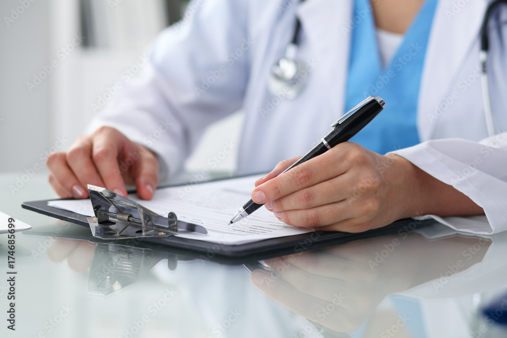 Fototapeta premium Doctor woman filling up medical form while sitting at the table, close-up of hands