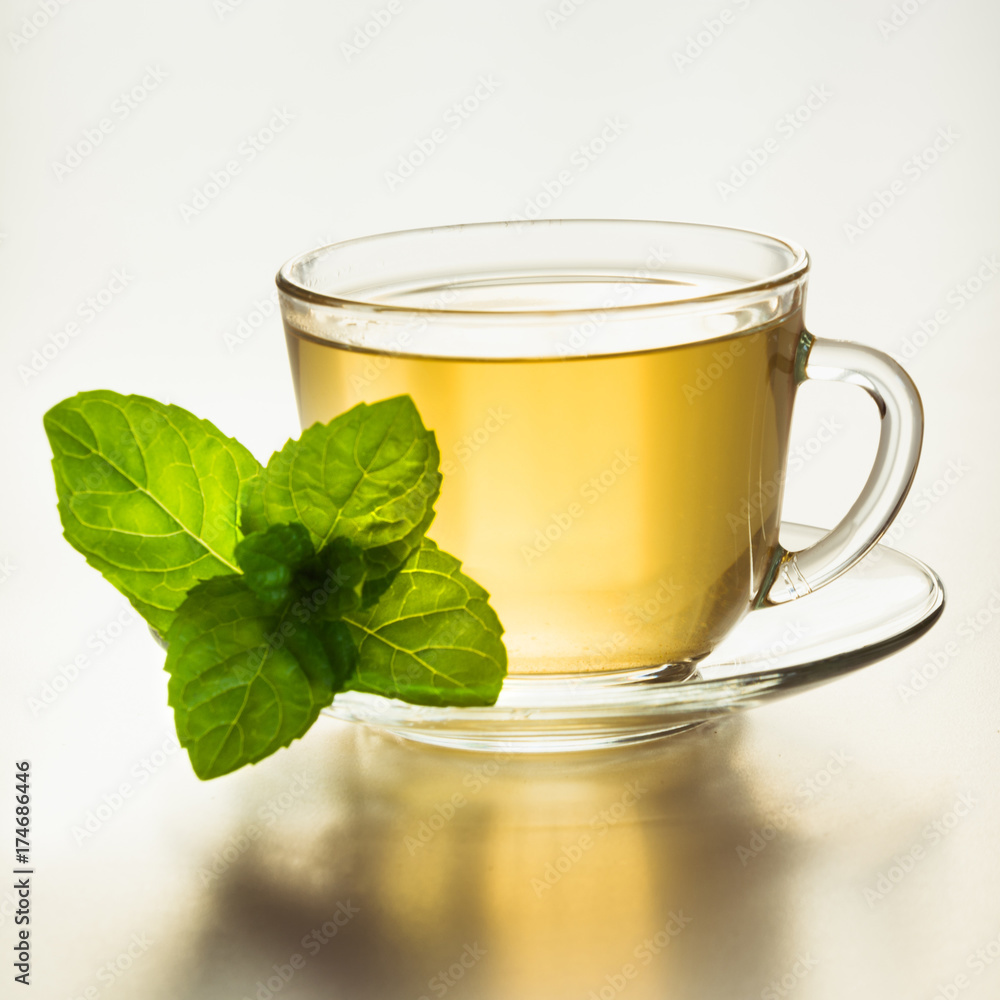 Glass cup of green tea and mint leaves on white. Glass cup of green tea and mint leaves on white.