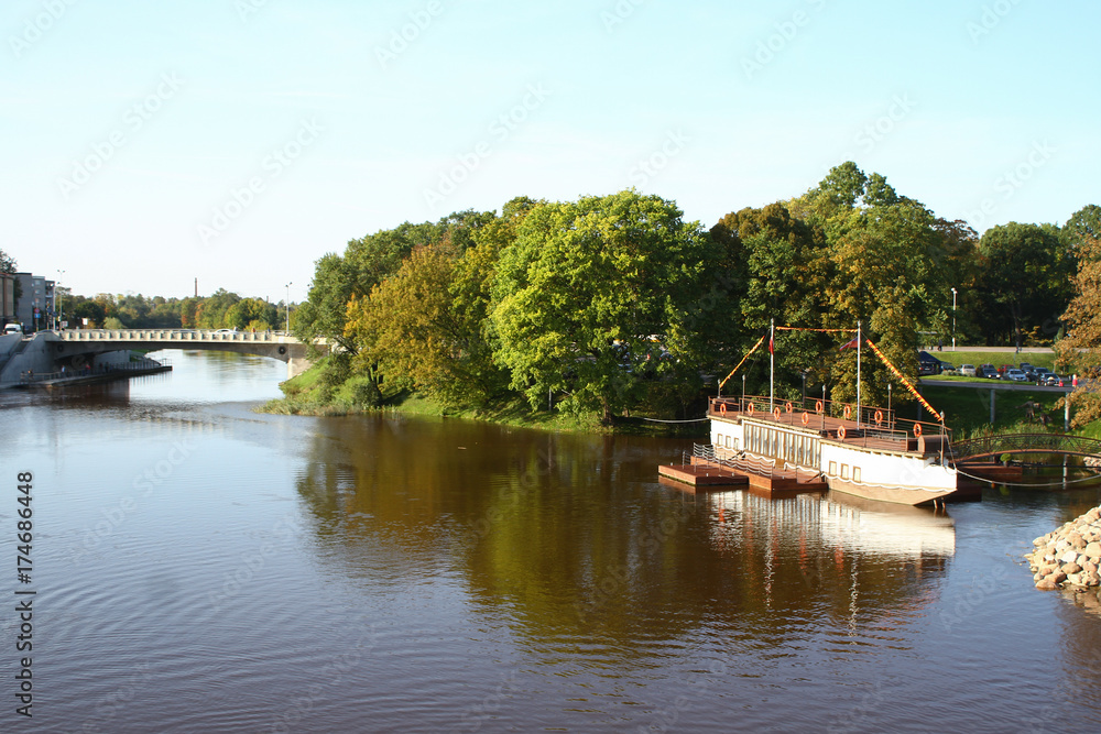 Riverside view with park, trees and small boat restaurant.