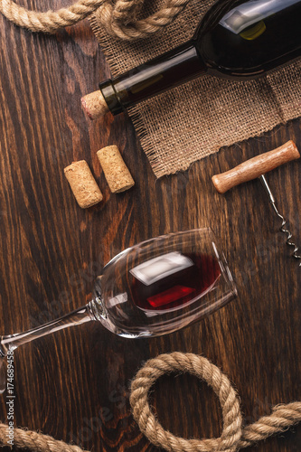 Glass with wine, bottle, corkscrew and burlap, top view