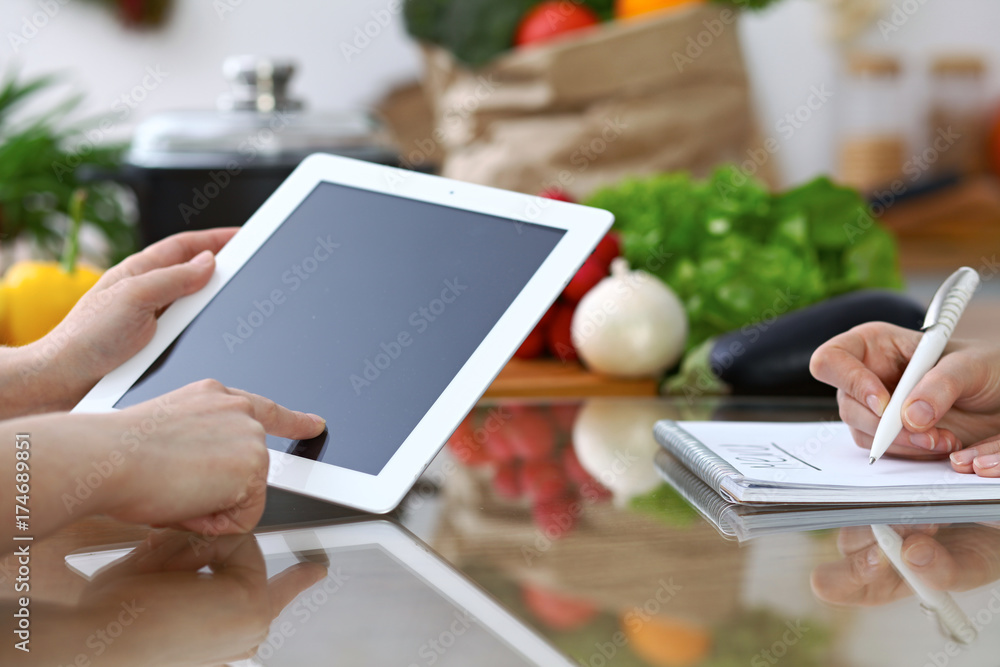 Close-up of  human hands are gesticulate over a tablet in the kitchen. Friends having fun while choosing menu or making online shopping