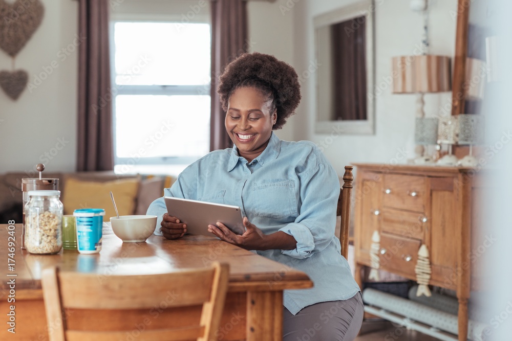 Smiling woman using a tablet while eating breakfast at home Smiling woman using a tablet while eating breakfast at home