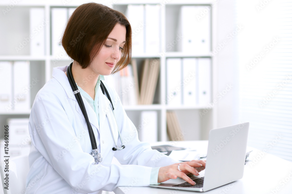 Young brunette female doctor sitting at the table and working at hospital office. Young brunette female doctor sitting at the table and working at hospital office.