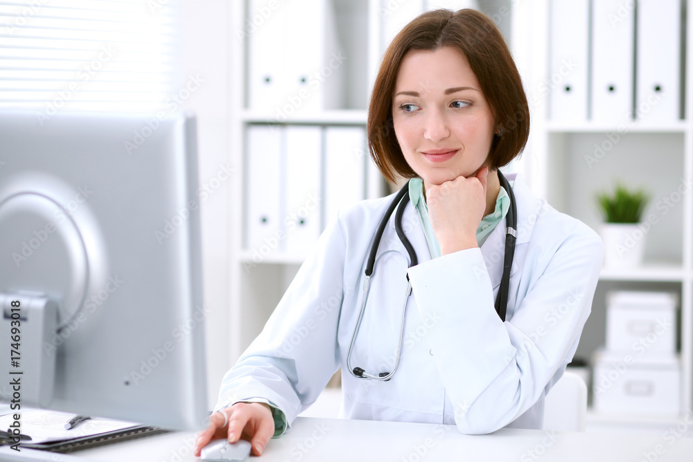 Young brunette female doctor sitting at the table and working at hospital office. Young brunette female doctor sitting at the table and working at hospital office.
