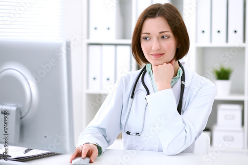 Young brunette female doctor sitting at the table and working at hospital office. 