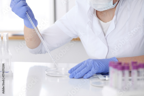 Close-up of professional female scientist in protective eyeglasses making experiment with reagents in laboratory. Medicine and research concept