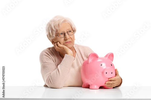 Pensive elderly woman with a piggybank seated at a table