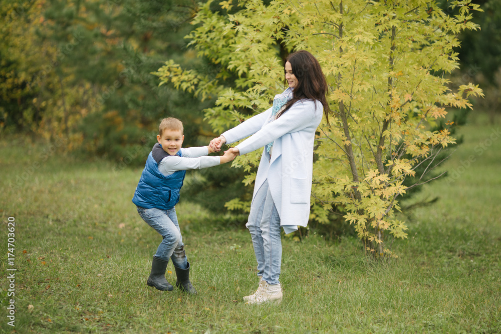 young mother and her son play in the autumn in the park, they are warmly dressed