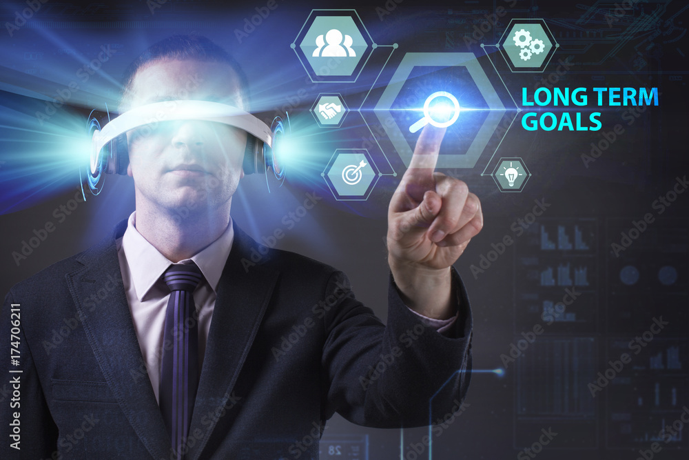 Business, Technology, Internet and network concept. Young businessman working in virtual reality glasses sees the inscription: Long term goals Business, Technology, Internet and network concept. Young businessman working in virtual reality glasses sees the inscription: Long term goals