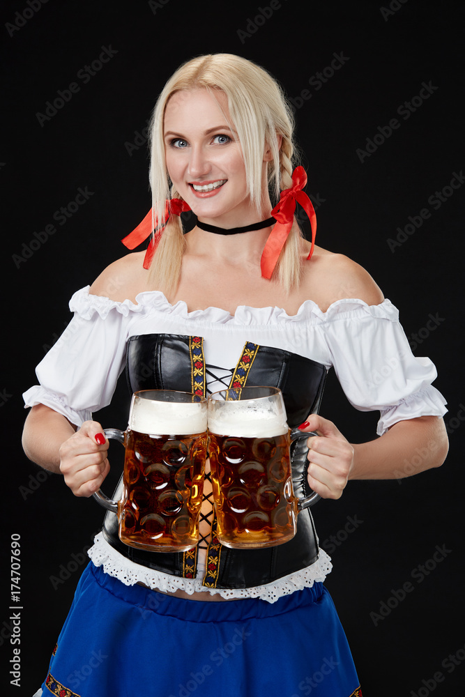 Young sexy woman wearing a dirndl with two beer mugs on black background Young sexy woman wearing a dirndl with two beer mugs on black background