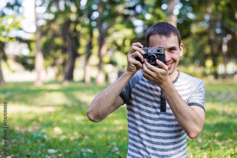 Young man taking pictures on retro camera in city park