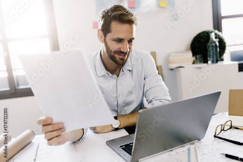 Smiling architect looking at laptop in his office