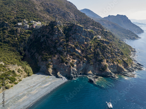 Vista aerea di Nonza e torre su una scogliera a picco sul mare. Spiaggia nera e mare. Catamarano ormeggiato. Penisola di Cap Corse, Corsica. Tratto di costa. Francia