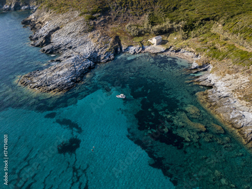 Vista aerea di una barca ormeggiata che galleggia su un mare trasparente. Piccola casa sulla costa rocciosa del Cap Corse. Vacanze estive. Coste della Corsica, spiagge e rocce