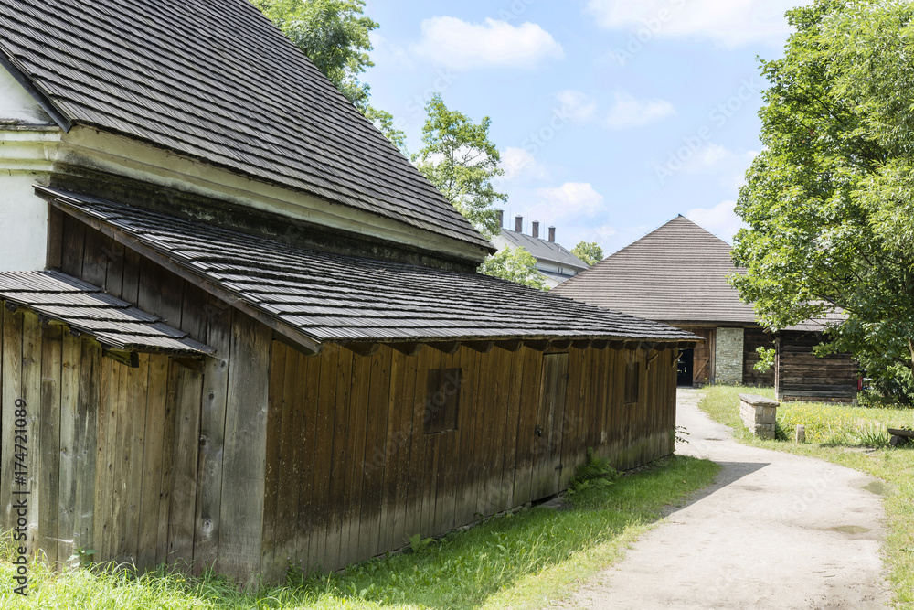 The wooden part of the building with a shallow roof in the village and a blue sky with clouds. The wooden part of the building with a shallow roof in the village and a blue sky with clouds.