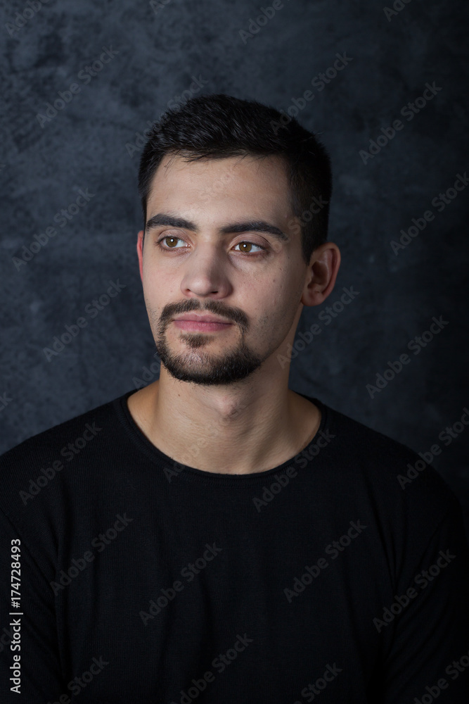 portrait of a young man on a dark background. A brunette, a white man, dressed in all dark. short beard and mustache. Emotions.