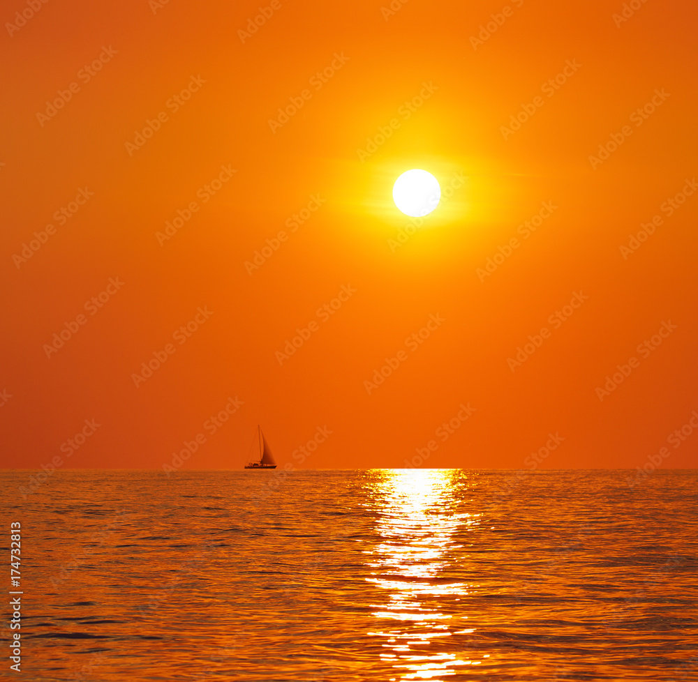 Sunset or sunrise over the sea. On the horizon a yacht.