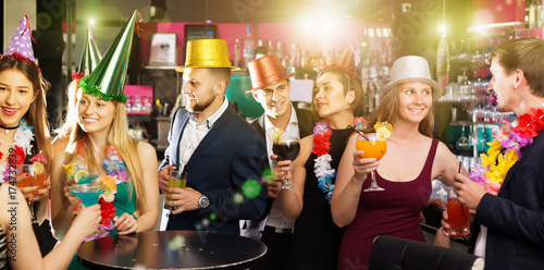 Portrait of happy women and men in caps with cocktails