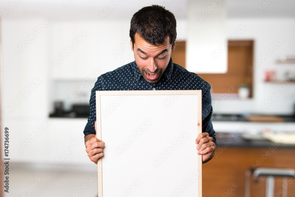 Surprised Brunette man holding an empty placard inside house Surprised Brunette man holding an empty placard inside house
