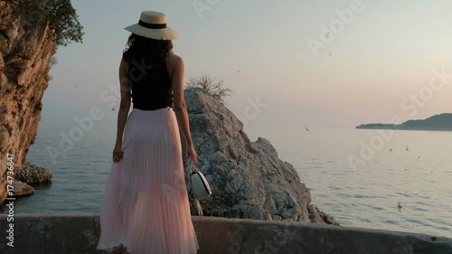 Woman in hat and pleated long skirt is walking along southern shore. photo
