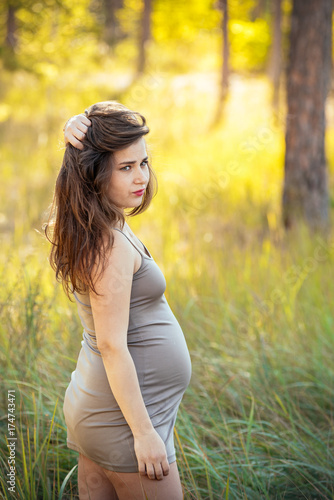 portrait of a beautiful young pregnant girl in a trendy dress against the background of an autumn forest