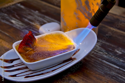 Fotografie Action shot of sugar caramelizing atop smooth crème brûlée under a chef’s torch