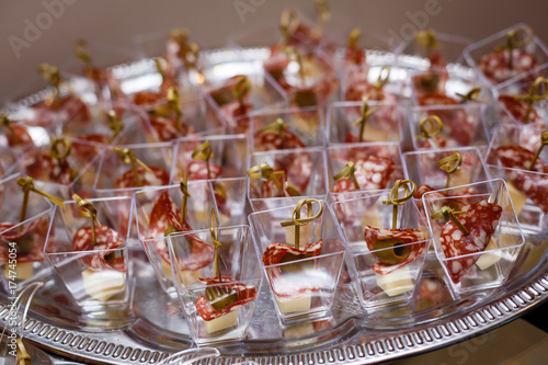 Catering for party. Close up of appetizers with cherry tomatoes, green olives, olive oil, cheese and spices in short glasses on wood brown table.