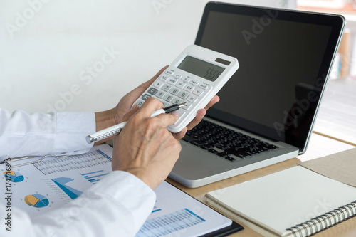 Female accountant calculations and analyzing financial graph data with calculator and laptop Business, Financing, Accounting, Doing finance, Economy, Savings Banking Concept