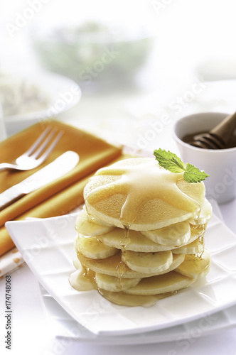 Homemade dessert, stack of pancakes with banana and topped with syrup on white dishes in morning.