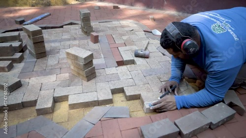 Using a level as a straight edge the brick paver artisan draws marks onto bricks that are in position for cutting for the two tone hardscaping design. photo