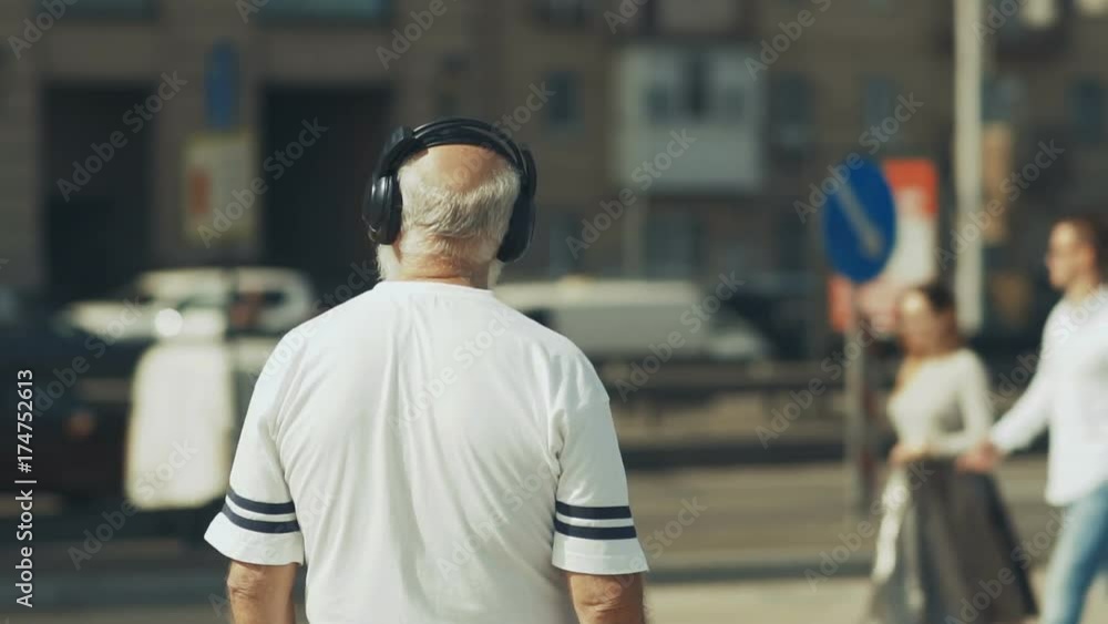Senior man in headphones looks on the urban road with cars Senior man in headphones looks on the urban road with cars