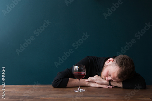 Drunk young male sleeping in bar. Unlucky date. Problems in adult ife, tired man with red wine on blue background with free space. Bad day, trouble in business concept