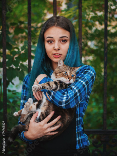 Young attractive punk girl with cat. Hipster with blue unusial dyed hair, piercing in nose, violet lenses and ears tunnels photo