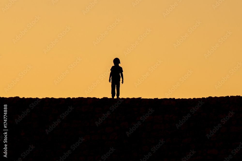 A kid silhouette standing on Kizkalesi castle while sunset
