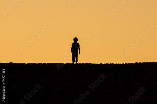 Fototapeta Naklejka Na Ścianę i Meble -  A kid silhouette standing on Kizkalesi castle while sunset