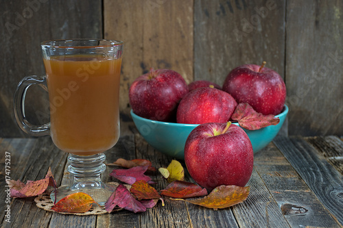 hot apple cider and red apples with autumn leaves on rustic barn wood