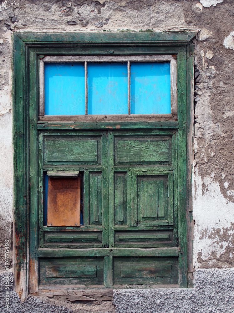 green half shuttered old shabby window in a decaying house with weathered wood and peeling paint set in a white flaking concrete wall green half shuttered old shabby window in a decaying house with weathered wood and peeling paint set in a white flaking concrete wall