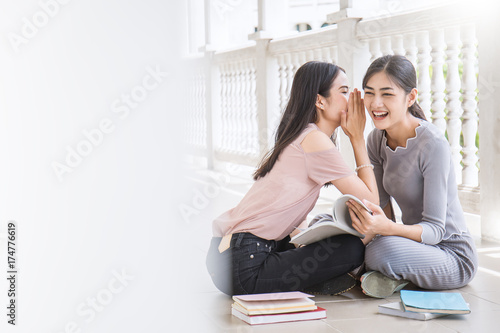 Asian student sitting outside school building reading book, Two asian girls wispering and gossipping while reading book together. Education concept photo