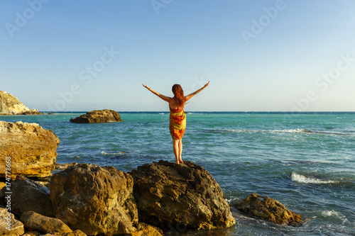 Young woman meets sea on the shore the Black Sea in Crimea, she is looking to the horizon. People freedom style. A girl heaved up hands. On a background the sea waves summer. Vacation.