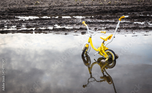 horizontal image of a broken yellow Child's bike stuck in a pool of water.