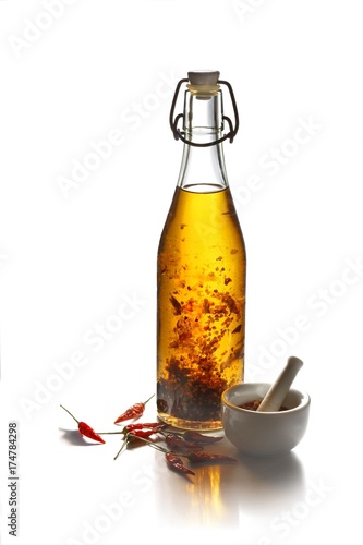 Chili oil with chilies in a bottle beside a mortar photo