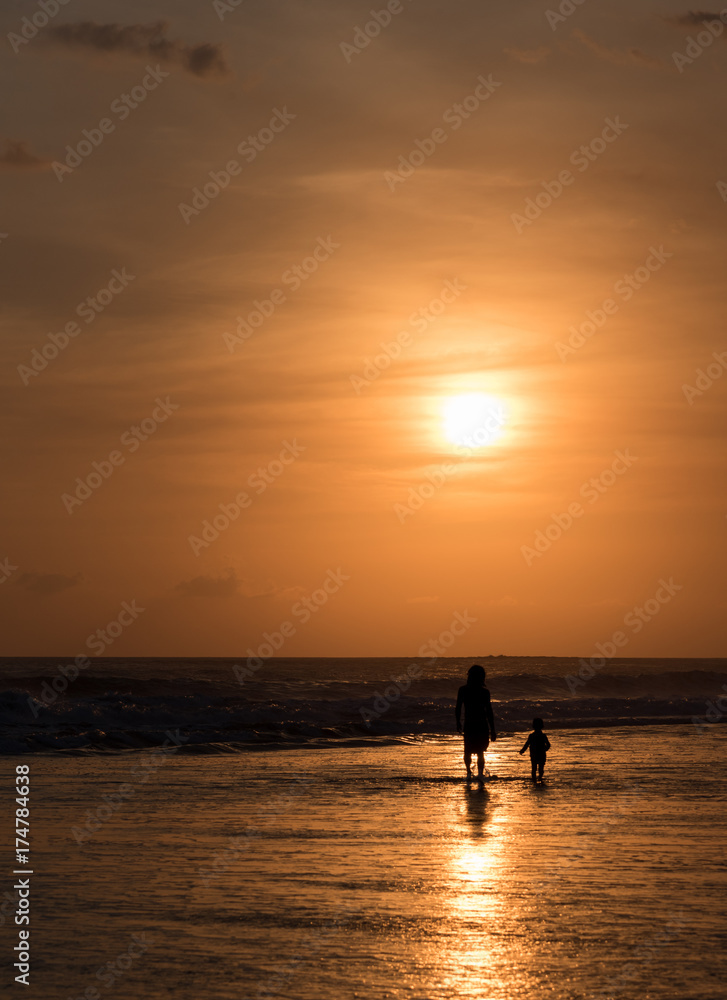 Silhouette of unrecognisable man and child at seaside on sunset
