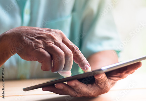 old man hold tablet with left hand and touch screen with right index finger on light brown wooden table surface © angyim